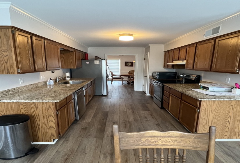 Kitchen featuring black appliances, ornamental molding, dark wood finished floors, light stone counters, and under cabinet range hood