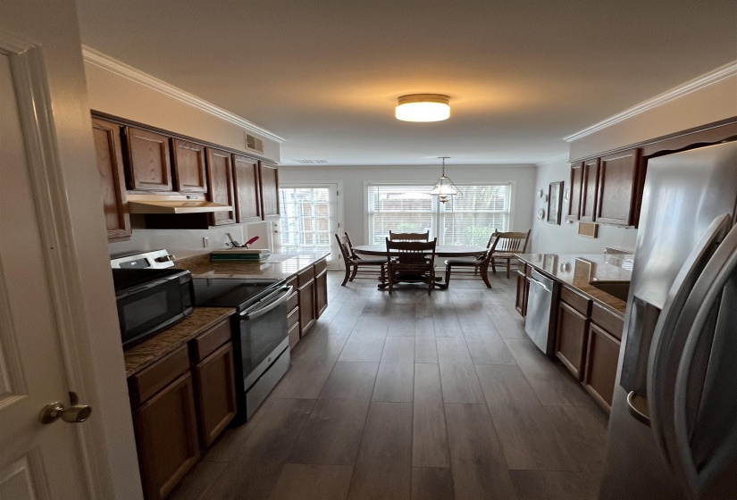 Kitchen featuring dark countertops, crown molding, appliances with stainless steel finishes, dark wood finished floors, and dark brown cabinets