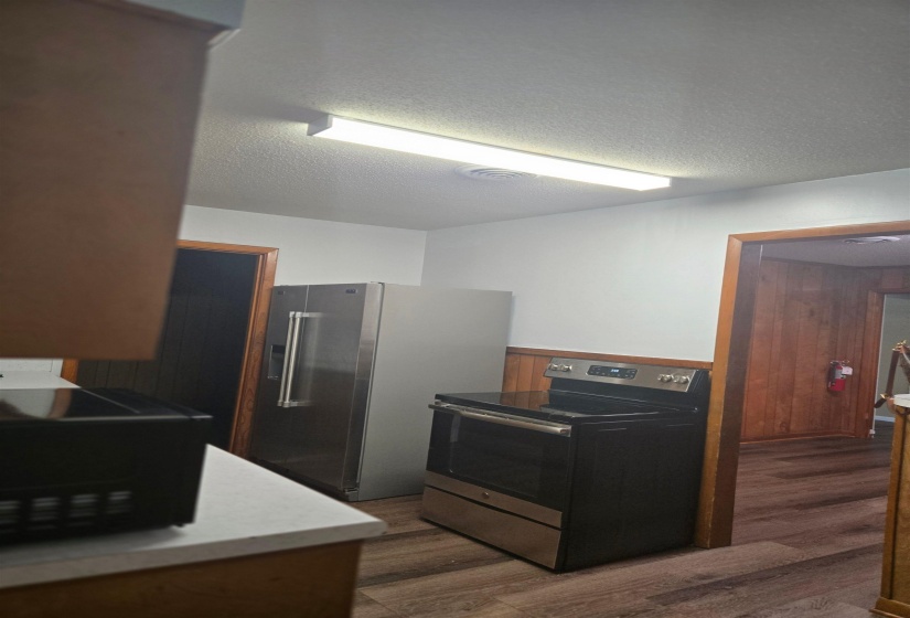 Kitchen featuring stainless steel appliances, dark wood-type flooring, a textured ceiling, a wainscoted wall, and wood walls