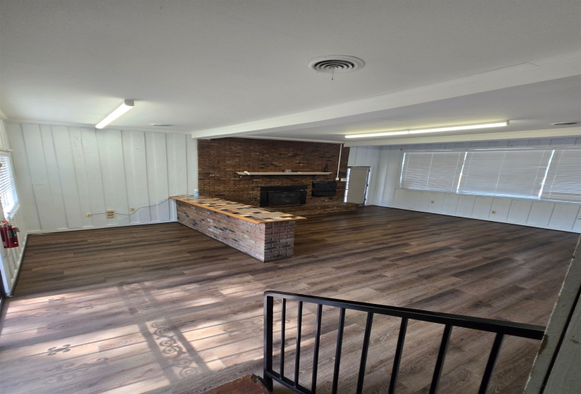 Unfurnished living room featuring dark wood-type flooring, a brick fireplace, and wood walls