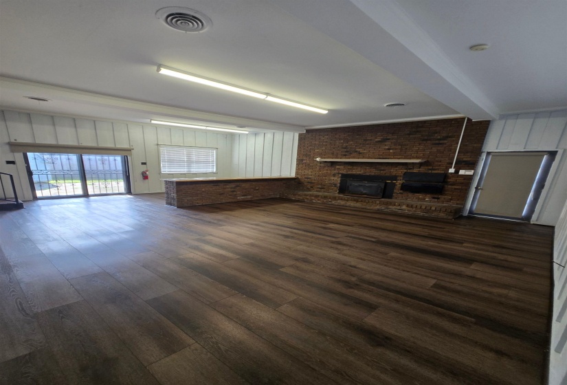 Unfurnished living room with brick wall, a brick fireplace, dark wood finished floors, and beamed ceiling