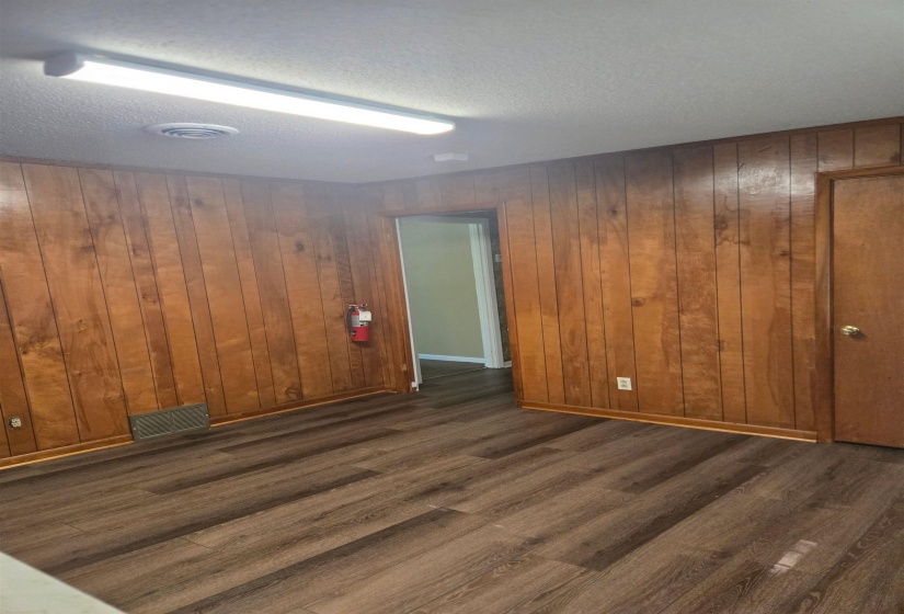 Empty room featuring wood walls, a textured ceiling, and dark wood-style flooring