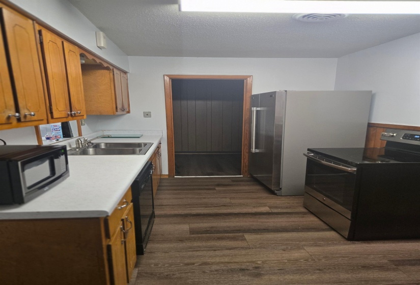 Kitchen featuring brown cabinetry, black appliances, a textured ceiling, light countertops, and dark wood-style floors