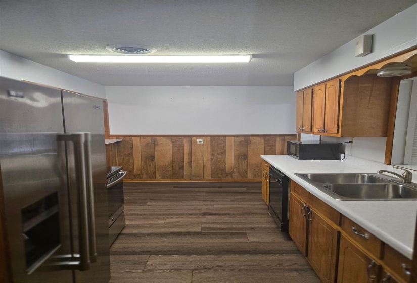 Kitchen featuring black appliances, wainscoting, light countertops, brown cabinetry, and wood walls