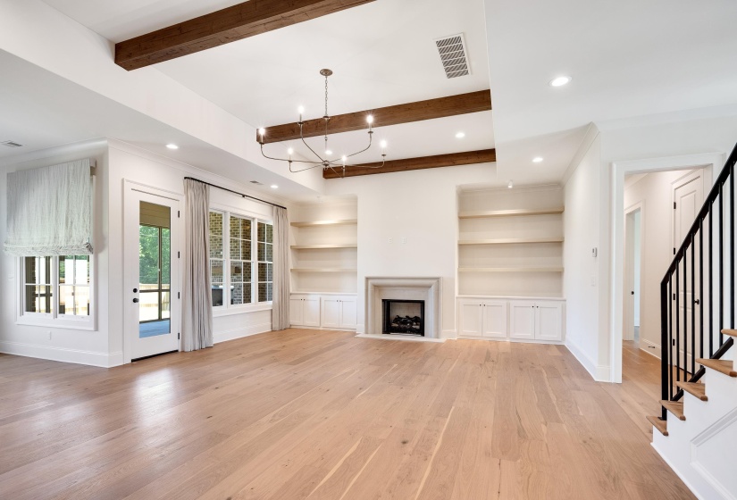 Unfurnished living room featuring light wood finished floors, baseboards, stairs, beamed ceiling, and built in features