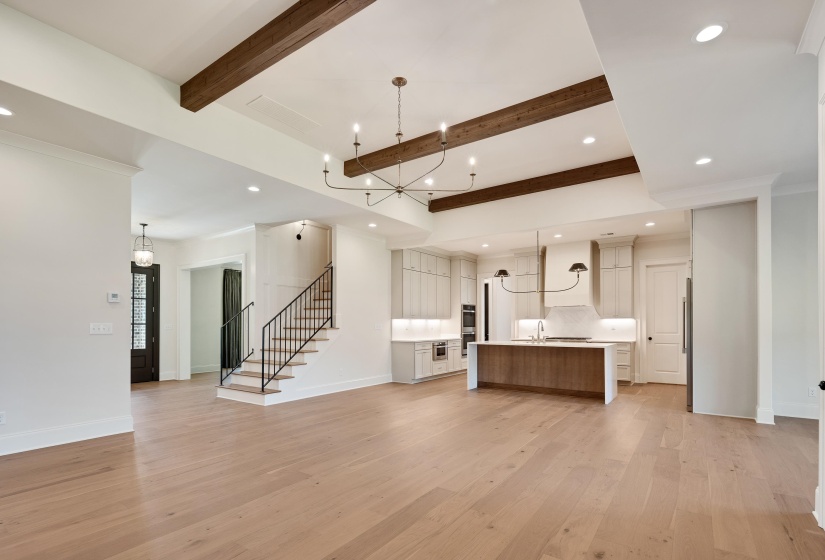 Unfurnished living room featuring beam ceiling, light wood-style flooring, a chandelier, recessed lighting, and baseboards