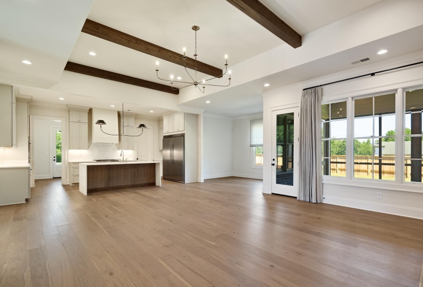 Unfurnished living room featuring a chandelier, beamed ceiling, plenty of natural light, light wood-style flooring, and baseboards