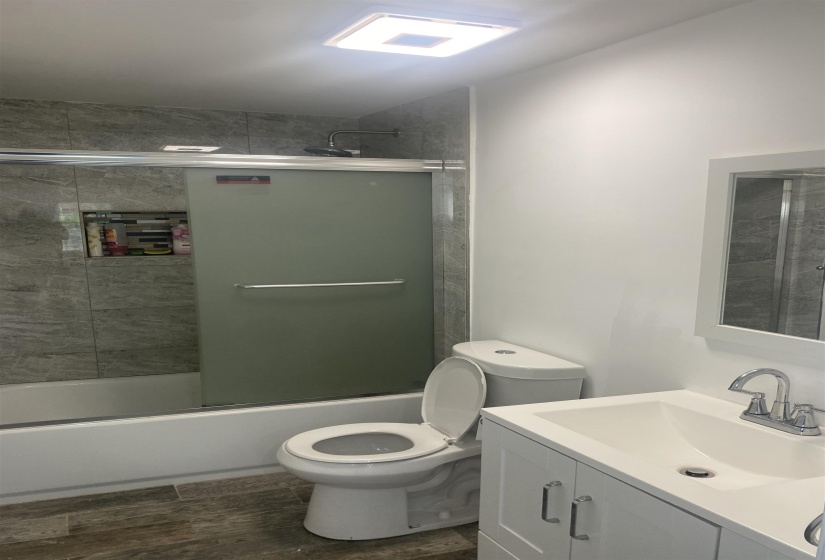 Bathroom with vanity, wood finished floors, toilet, and shower / bath combination with glass door