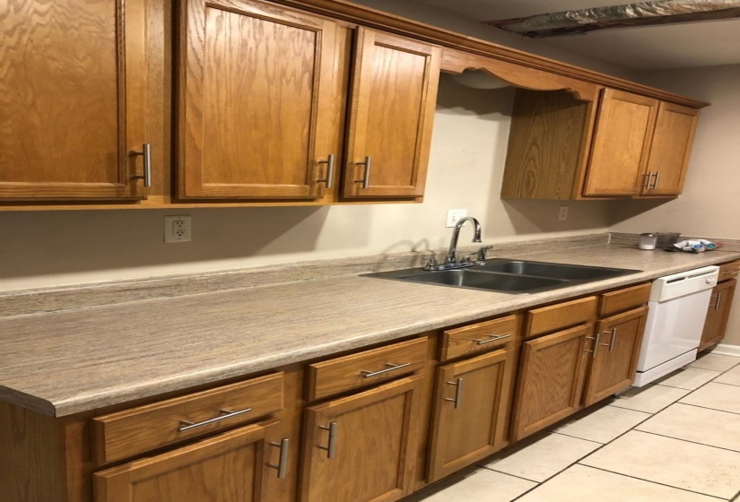 Kitchen with dishwasher, light tile patterned floors, brown cabinetry, and light countertops