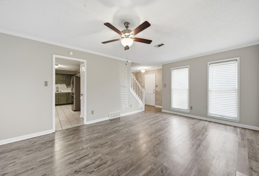 Unfurnished living room featuring ornamental molding, ceiling fan, light wood-style flooring, and stairs