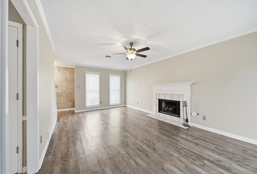 Unfurnished living room featuring ornamental molding, a tile fireplace, wood finished floors, and a ceiling fan