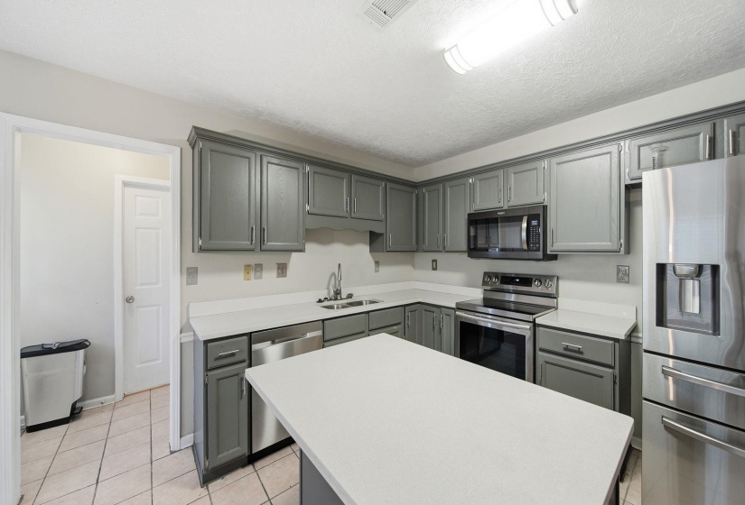 Kitchen featuring gray cabinets, appliances with stainless steel finishes, light countertops, light tile patterned floors, and a kitchen island