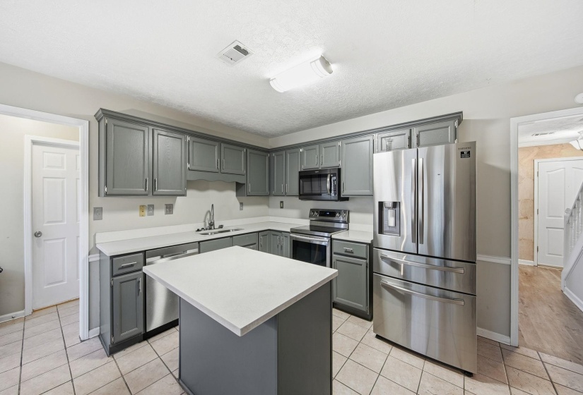 Kitchen with stainless steel appliances, gray cabinets, light countertops, a center island, and a textured ceiling