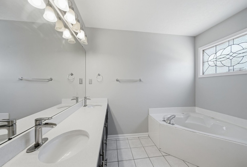 Full bath with double vanity, a garden tub, and light tile patterned floors