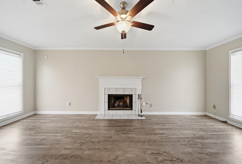 Unfurnished living room featuring plenty of natural light, a tiled fireplace, light wood-type flooring, ornamental molding, and ceiling fan