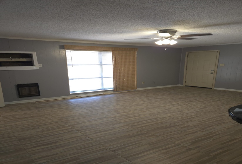 Unfurnished living room with a fireplace, heating unit, a textured ceiling, a ceiling fan, and wood walls