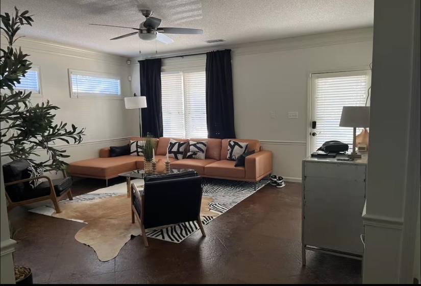 Living room featuring a textured ceiling, crown molding, a ceiling fan, and concrete flooring