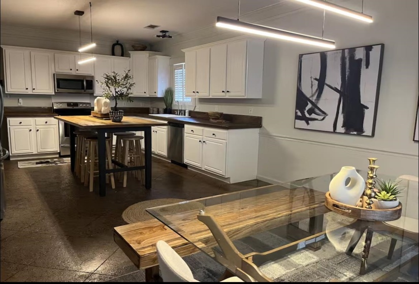 Kitchen with stainless steel appliances, hanging light fixtures, white cabinets, ornamental molding, and wooden counters
