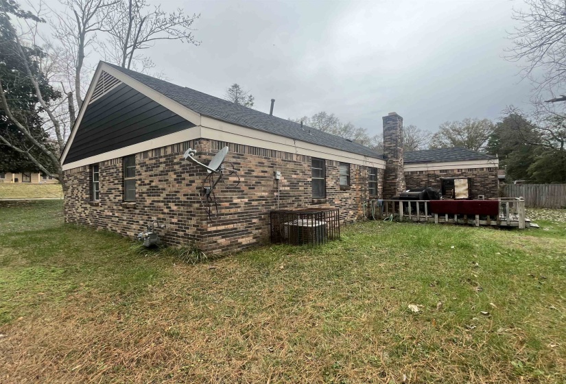 View of property exterior featuring a lawn, brick siding, a chimney, and a wooden deck