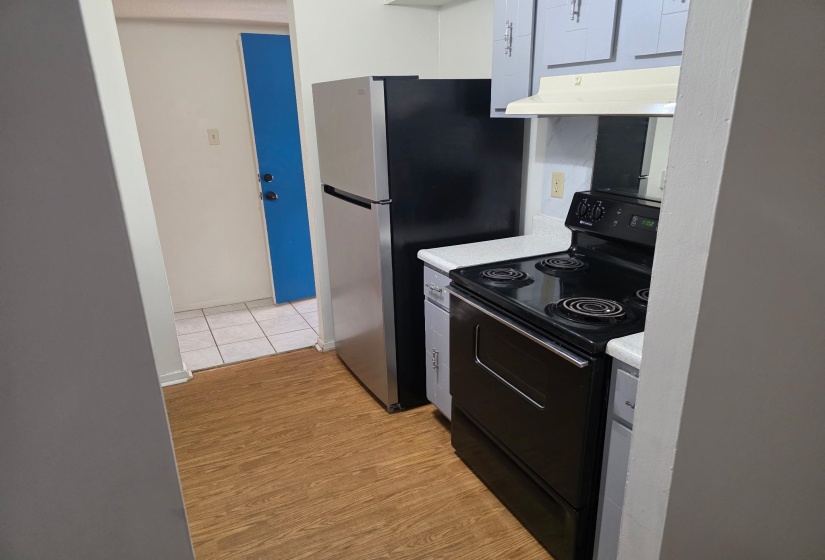 Kitchen with black electric range oven, light countertops, under cabinet range hood, light wood finished floors, and freestanding refrigerator