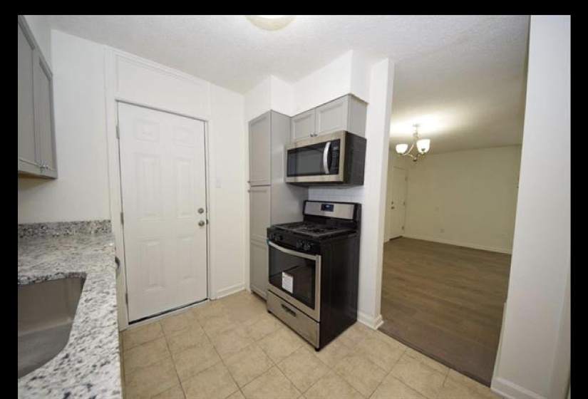 Kitchen with appliances with stainless steel finishes, a chandelier, light stone counters, gray cabinetry, and light tile patterned floors