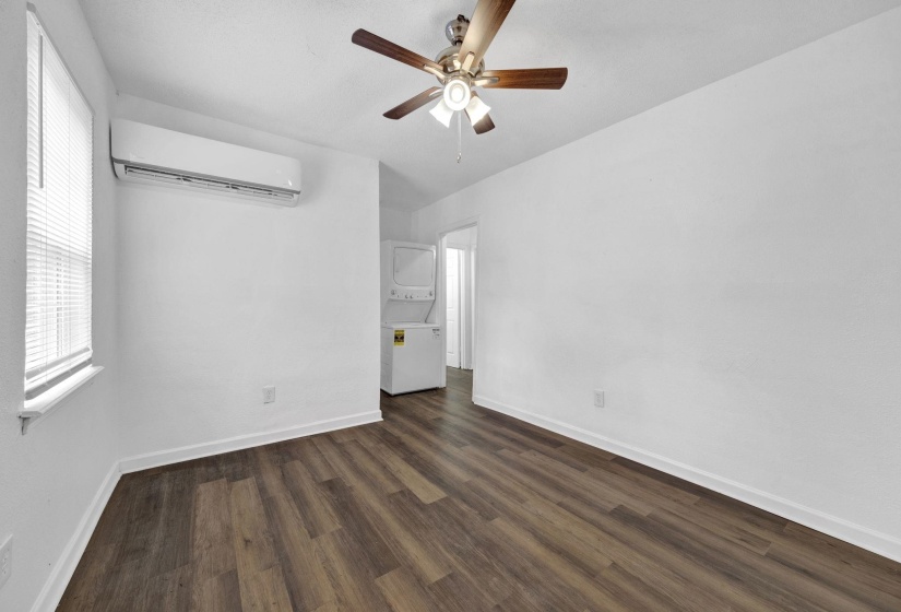 Unfurnished bedroom featuring stacked washer / dryer, an AC wall unit, dark wood-style flooring, and ceiling fan
