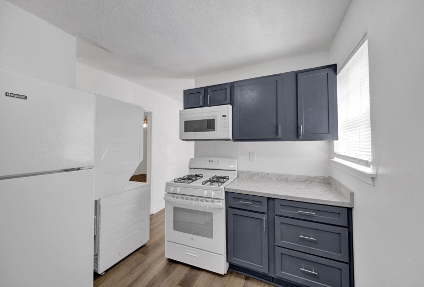Kitchen featuring white appliances, wood finished floors, light stone countertops, and gray cabinetry