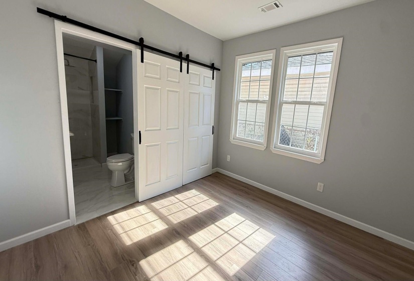 Unfurnished bedroom featuring a barn door, wood finished floors, ensuite bath, and a closet