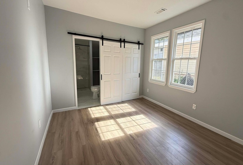 Unfurnished bedroom with a barn door, light wood-style flooring, and connected bathroom