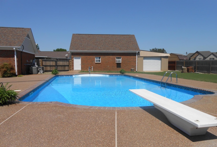 View of pool with a diving board, a fenced backyard, patio surround, and an outdoor structure