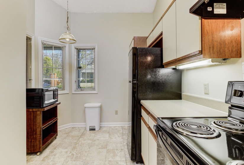 Kitchen featuring range with electric stovetop, pendant lighting, ventilation hood, light countertops, and black microwave