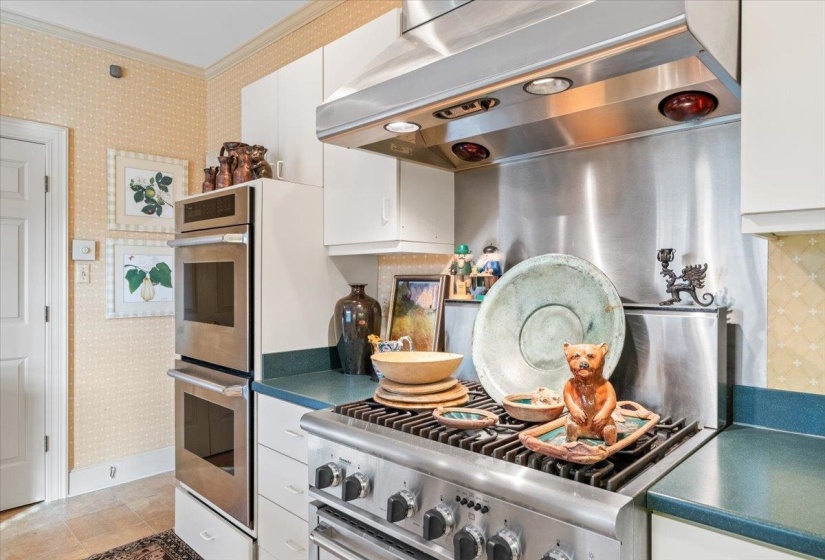 Kitchen with extractor fan, wallpapered walls, dark countertops, white cabinetry, and ornamental molding