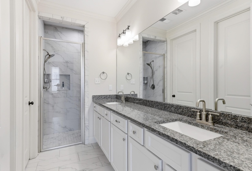 Full bath with light marble finish floors, a nice sized shower, double vanity, and ornamental molding