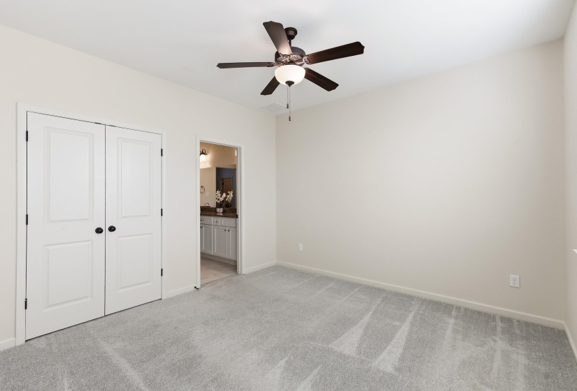 Upstairs bedroom featuring light colored carpet, a double closet, a ceiling fan, and ensuite bathroom