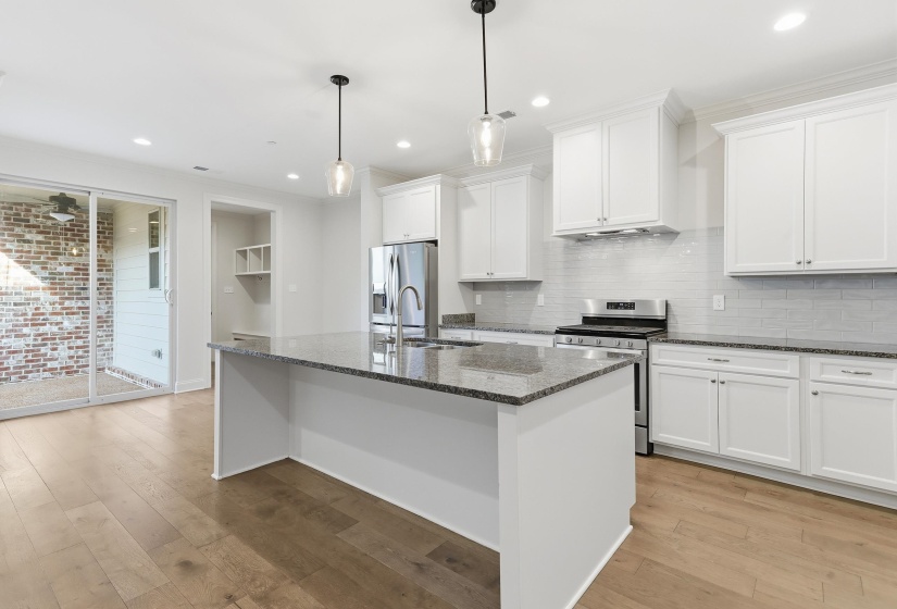 Kitchen featuring white cabinetry, stainless steel appliances, an island with sink, tasteful backsplash, and stone counters