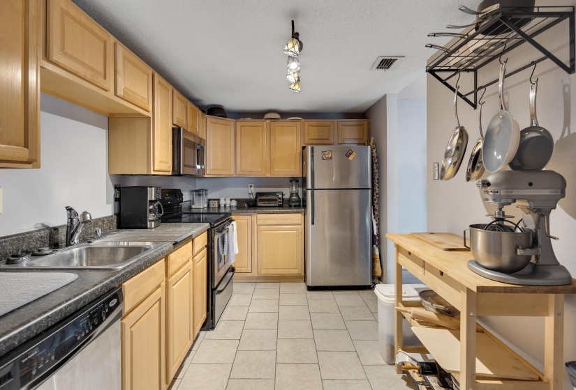 Kitchen featuring dark countertops, appliances with stainless steel finishes, light tile patterned floors, a textured ceiling, and light brown cabinetry