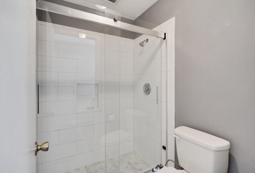 Full bath featuring a shower stall and a textured wall