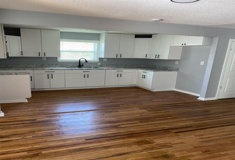Kitchen with a textured ceiling, white cabinets, dark wood-style flooring, and light stone countertops