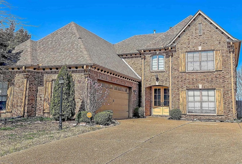 French country inspired facade with roof with shingles, brick siding, driveway, a garage, and french doors