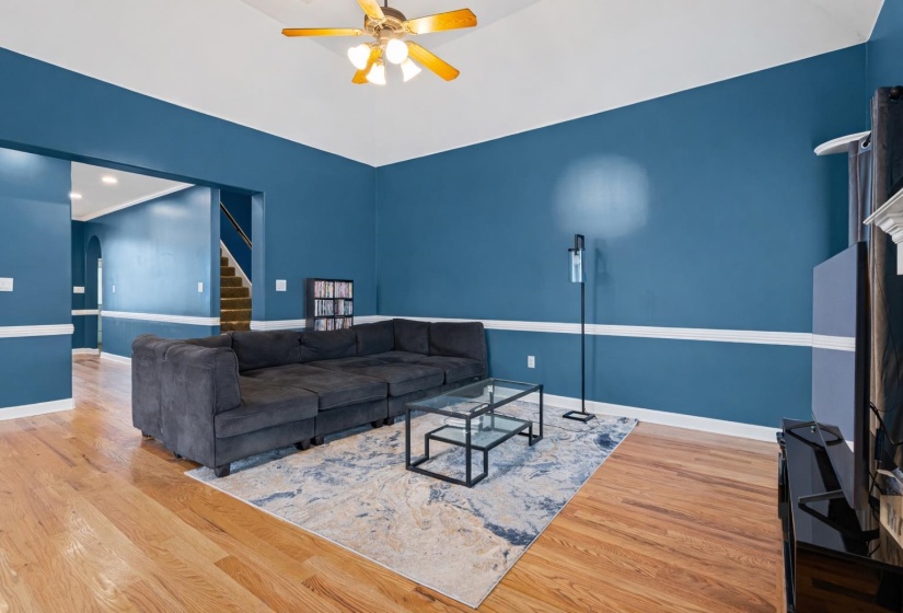 Living room featuring arched walkways, a ceiling fan, light wood-type flooring, stairs, and vaulted ceiling