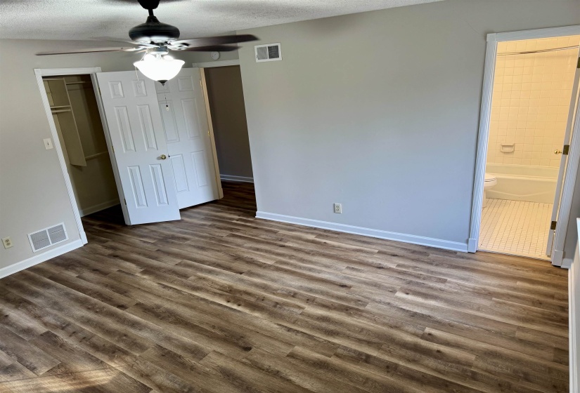 Unfurnished bedroom featuring a closet, a textured ceiling, ceiling fan, dark wood-style flooring, and ensuite bathroom