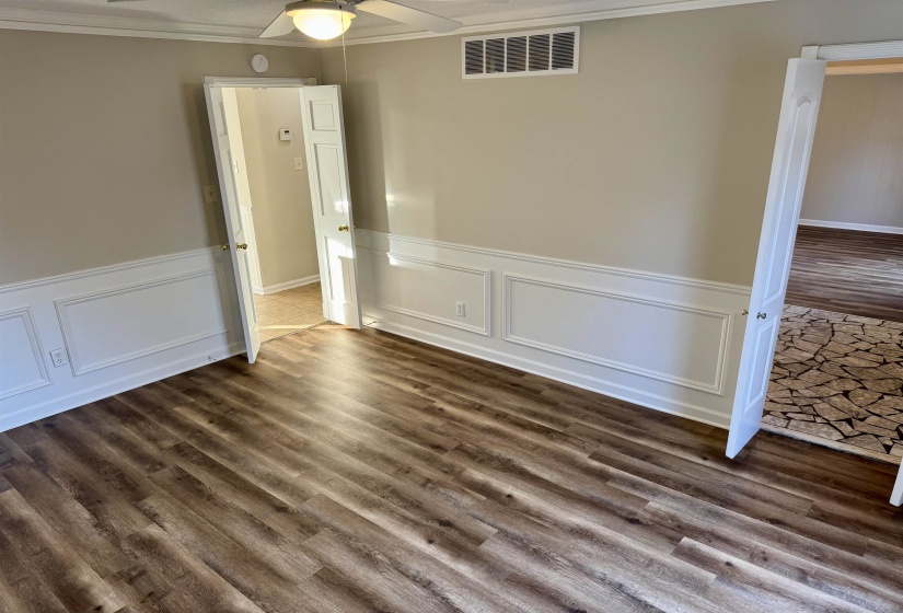 Spare room with a wainscoted wall, dark wood-type flooring, a decorative wall, crown molding, and a ceiling fan
