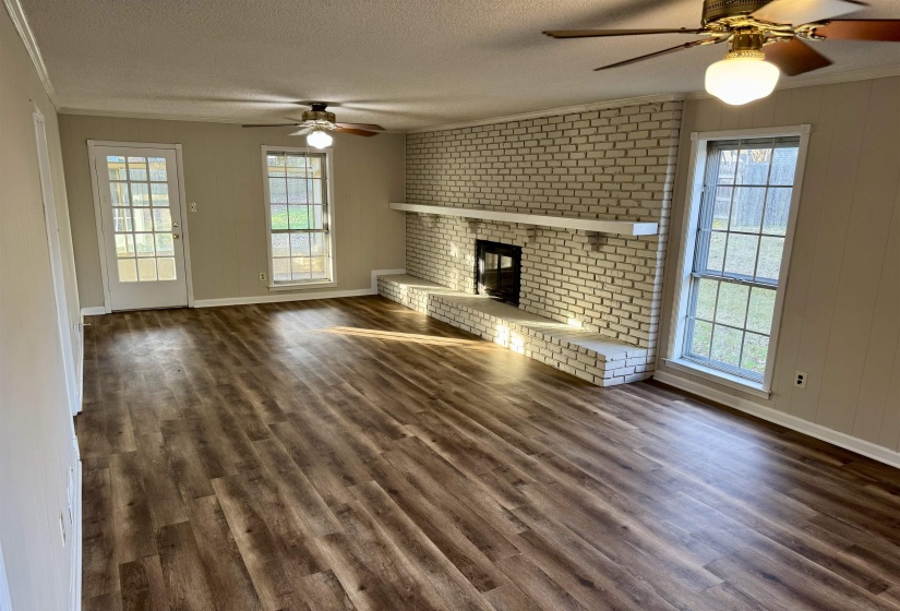 Unfurnished living room with a ceiling fan, ornamental molding, a fireplace, a textured ceiling, and dark wood finished floors