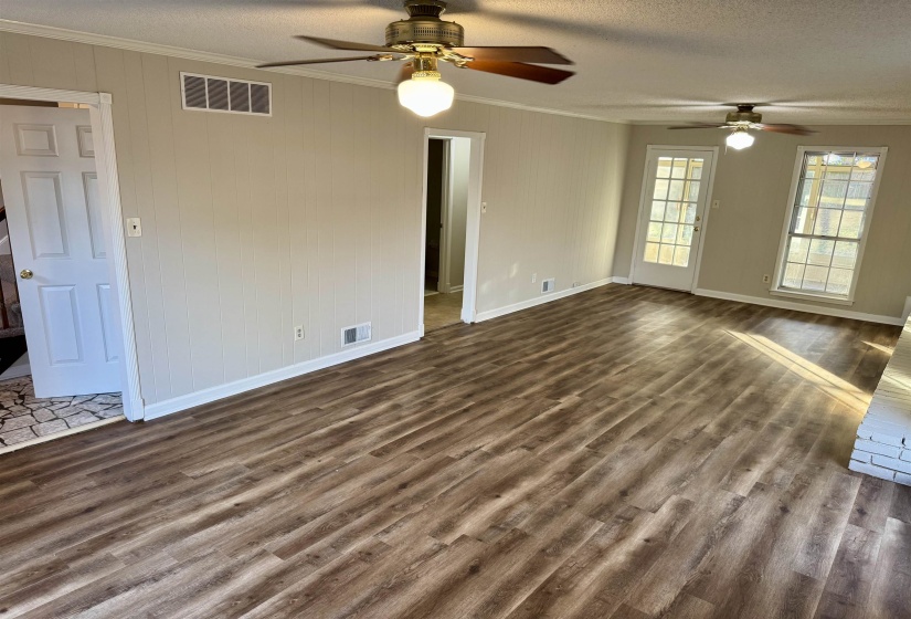 Unfurnished living room with dark wood-style floors, ornamental molding, a textured ceiling, a ceiling fan, and wooden walls