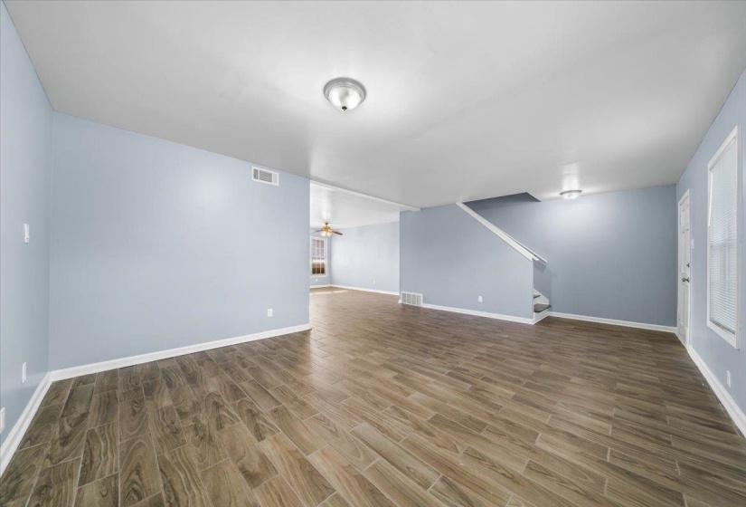 Unfurnished living room with wood tiled floors, a ceiling fan, and stairs