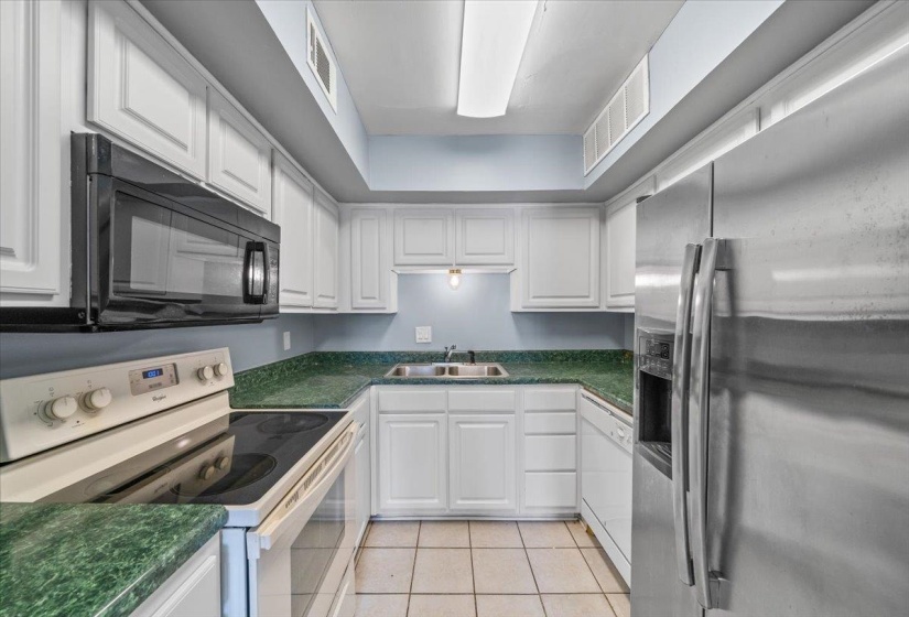 Kitchen featuring white appliances, white cabinets, dark countertops, and light tile patterned flooring