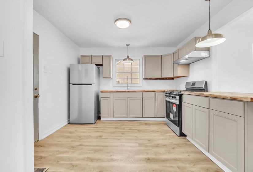 Kitchen with pendant lighting, appliances with stainless steel finishes, light wood-type flooring, and butcher block counters