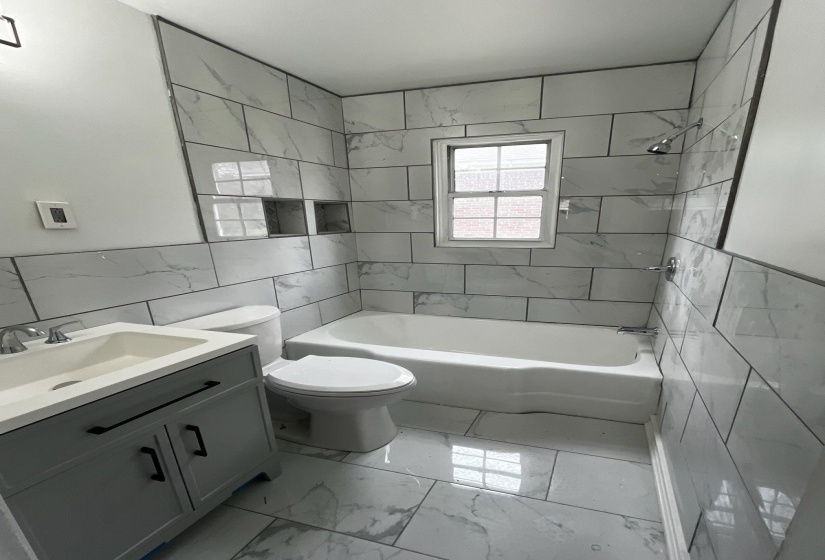 Bathroom featuring tile walls, light marble finish floors, shower / bathtub combination, vanity, and a wainscoted wall