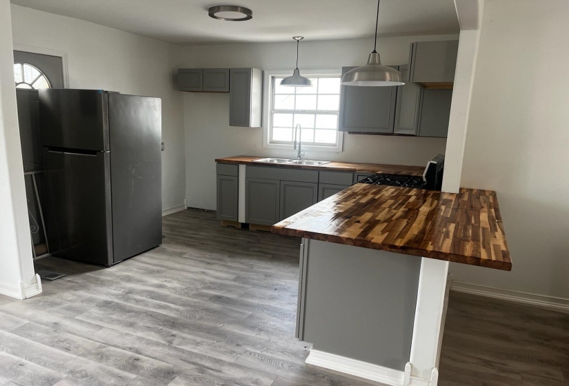 Kitchen featuring butcher block counters, gray cabinetry, freestanding refrigerator, and a peninsula