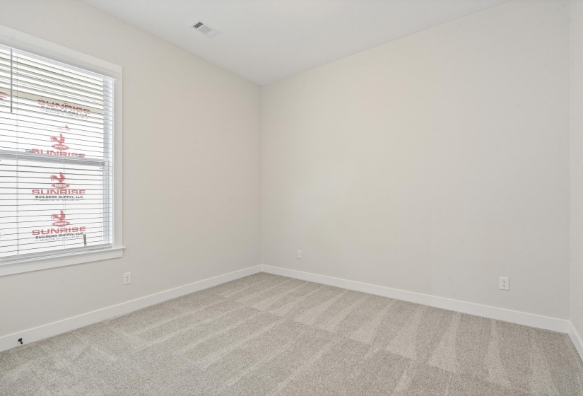 Bright room featuring a window with horizontal blinds, neutral wall tones, and gray patterned carpeting
